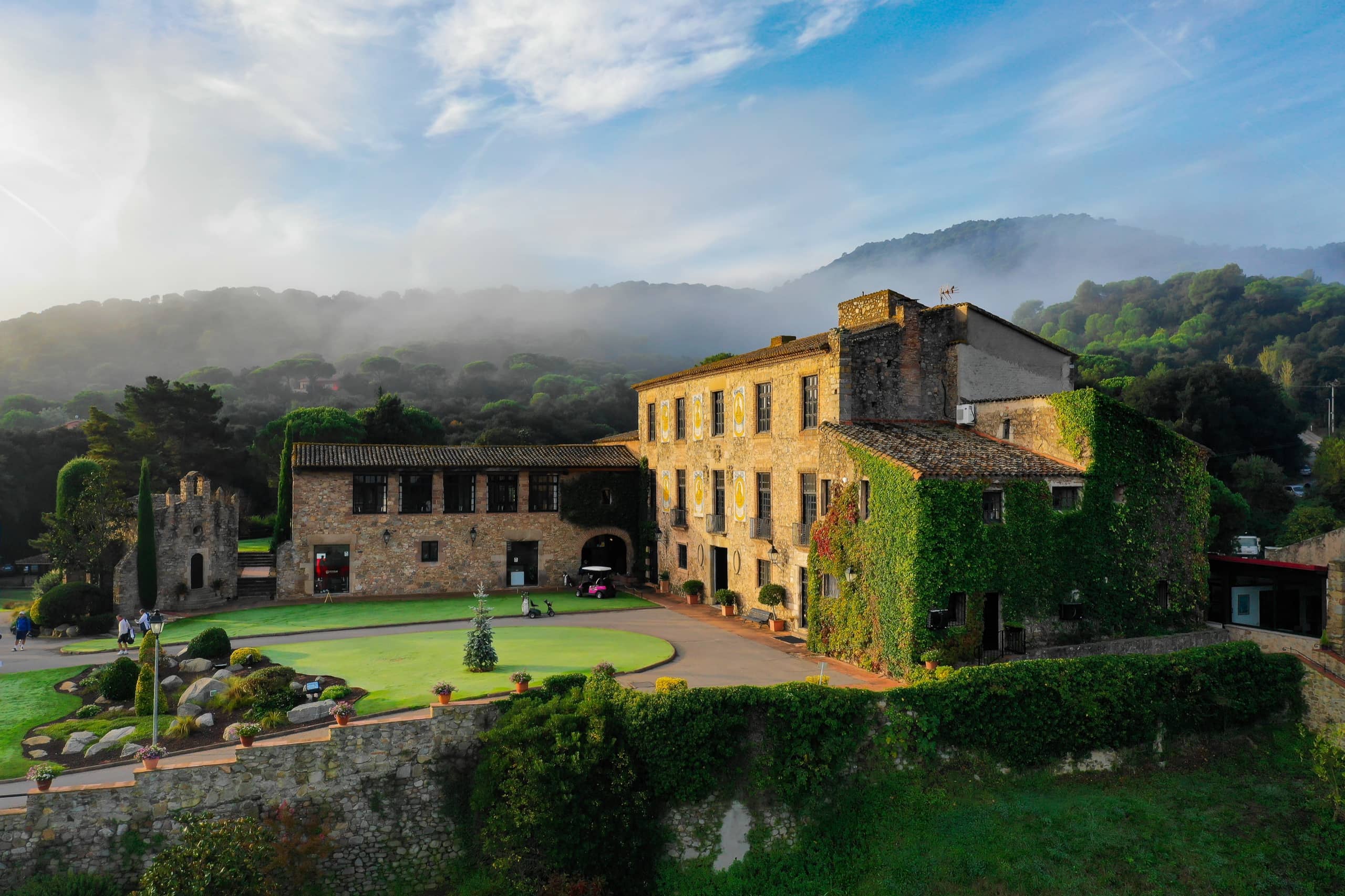 Castillo con jardín entre montañas y niebla matinal