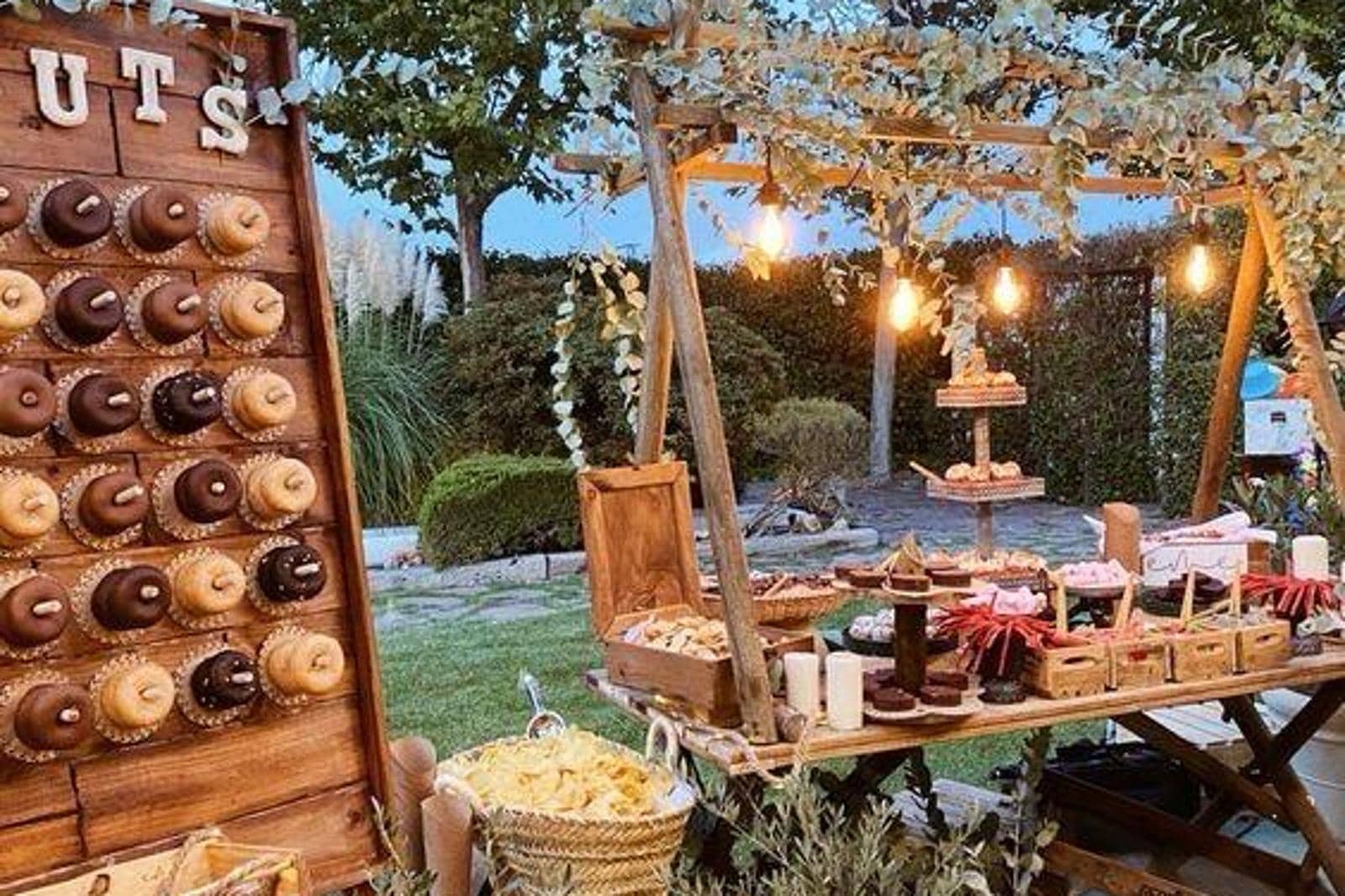 Mesa de dulces con muro de donuts y guirnaldas de luces al aire libre