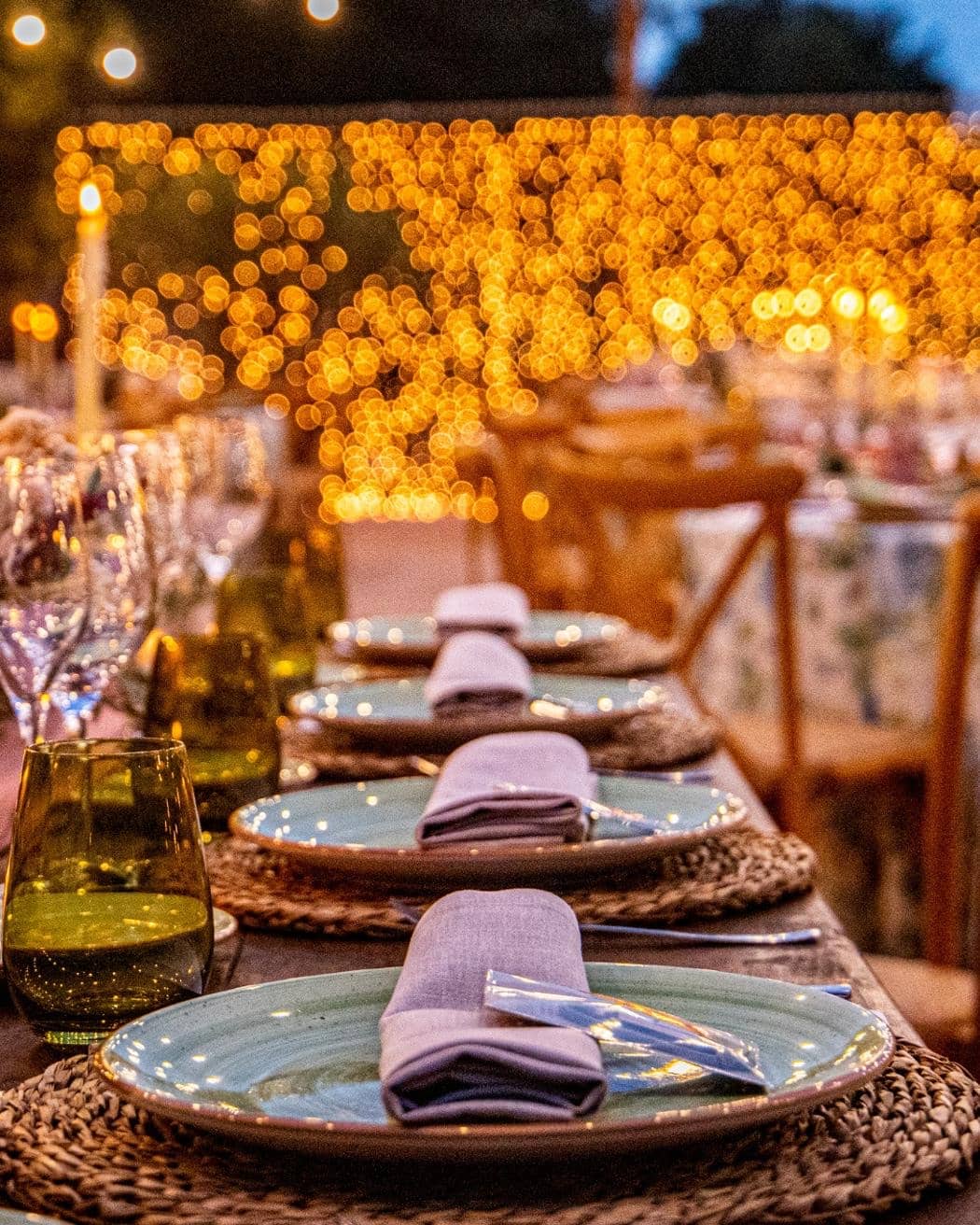 Mesa con velas, platos y servilletas malva bajo luces cálidas