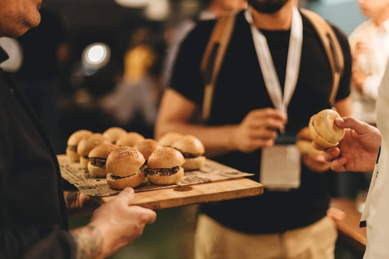 Camarero sirviendo una bandeja de mini hamburguesas en un cóctel