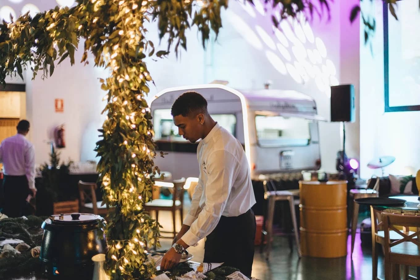 Camarero preparando el servicio junto a un arco de vegetación y luces